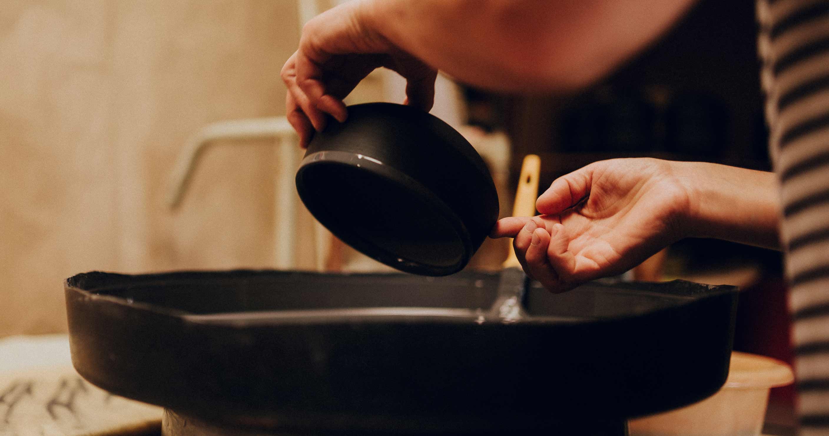 A woman glazing the outside of a small matte black ceramic bowl