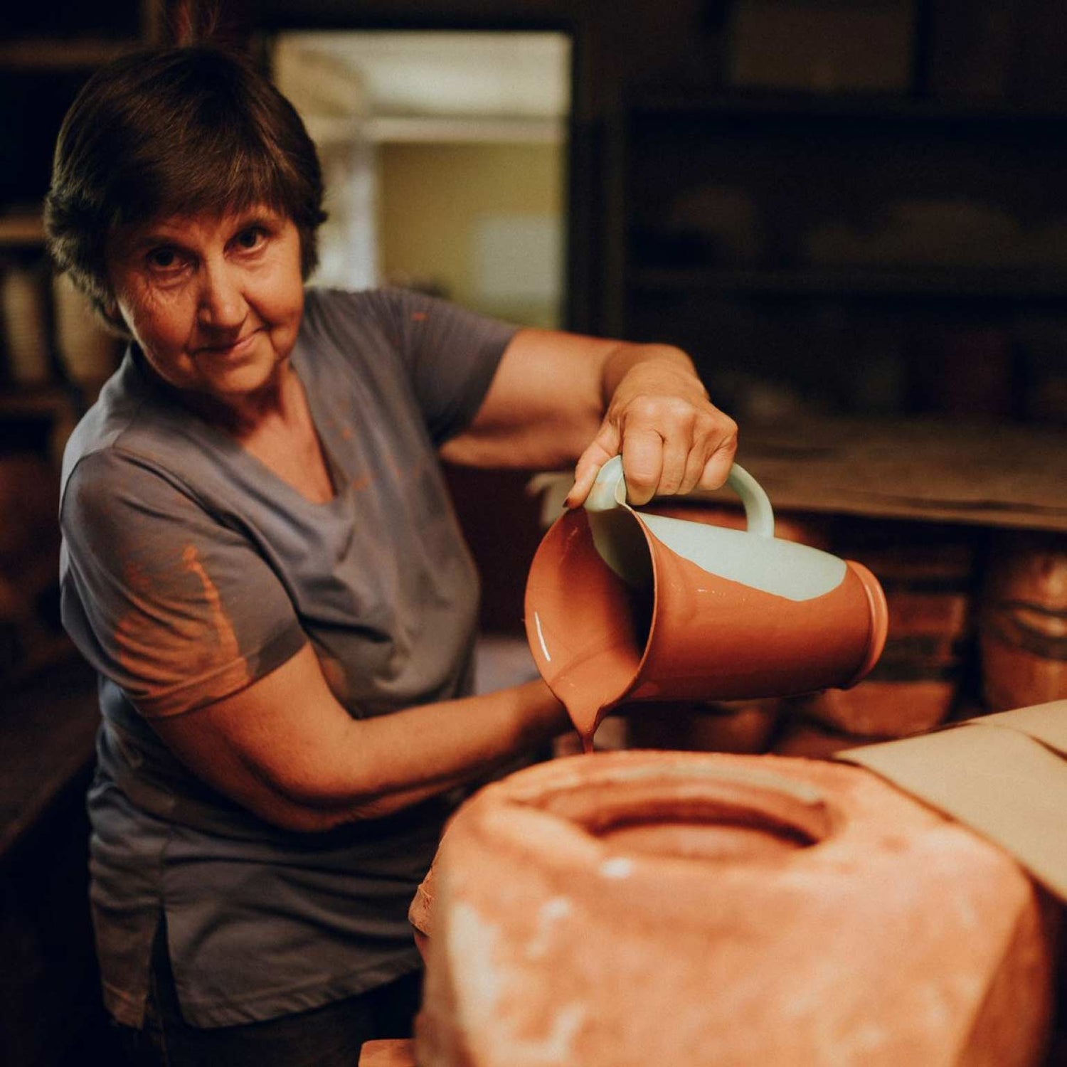 A woman using a pitcher to glaze a ceramic dish